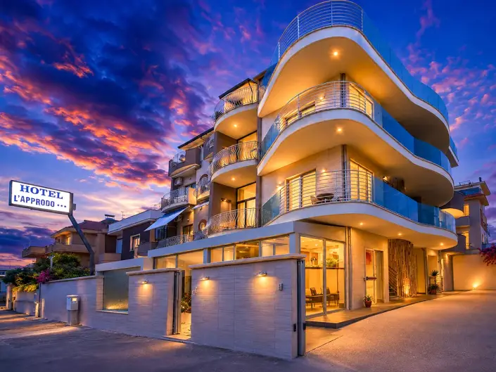 Modern hotel with a stylish façade, glowing lights, and a vibrant sunset sky. Inviting entrance and balconies visible.